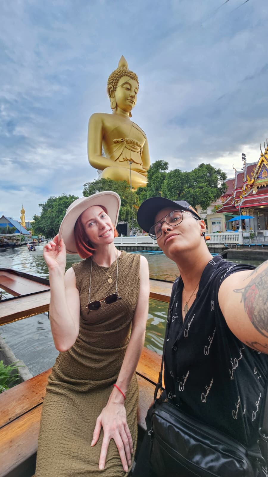 Clare and Aurita on a boat in Bangkok with the giant Buddha at Wat Paknam behind them